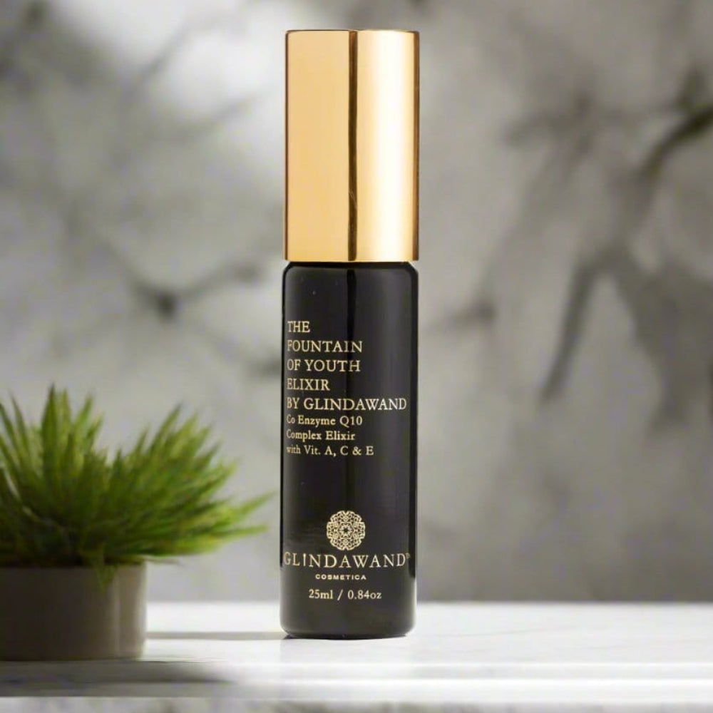 A cosmetics product with a black and gold packaging, possibly a face elixir or serum, displayed on a surface with a plant in the background.